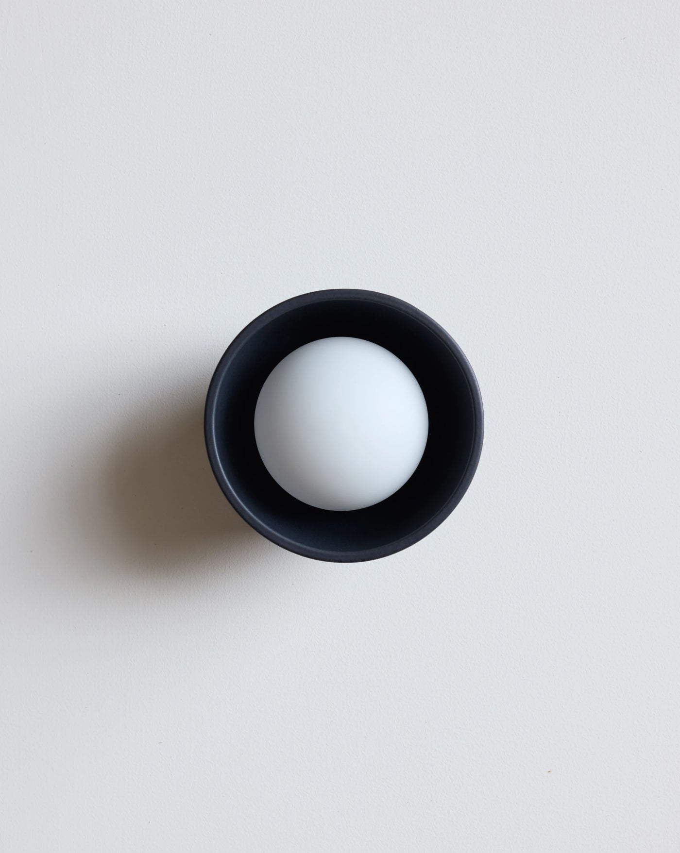 A minimalist black blue ceramic sconce photographed on a clean, light gray background.