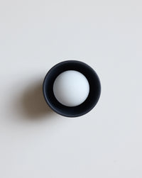A minimalist black blue ceramic sconce photographed on a clean, light gray background.