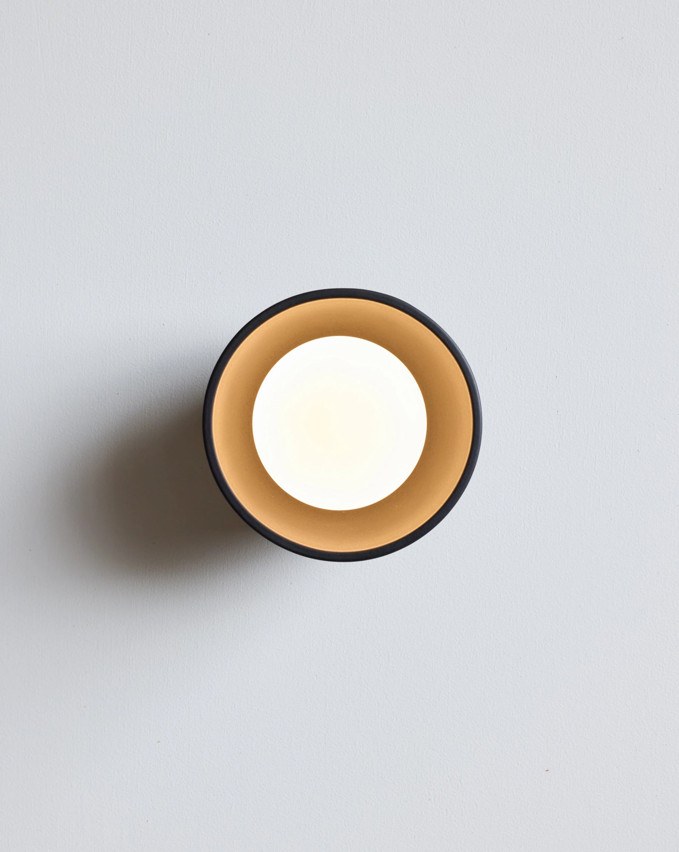 A minimalist wall sconce light fixture with a soft white light, set against a clean light gray background.