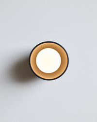 A minimalist wall sconce light fixture with a soft white light, set against a clean light gray background.