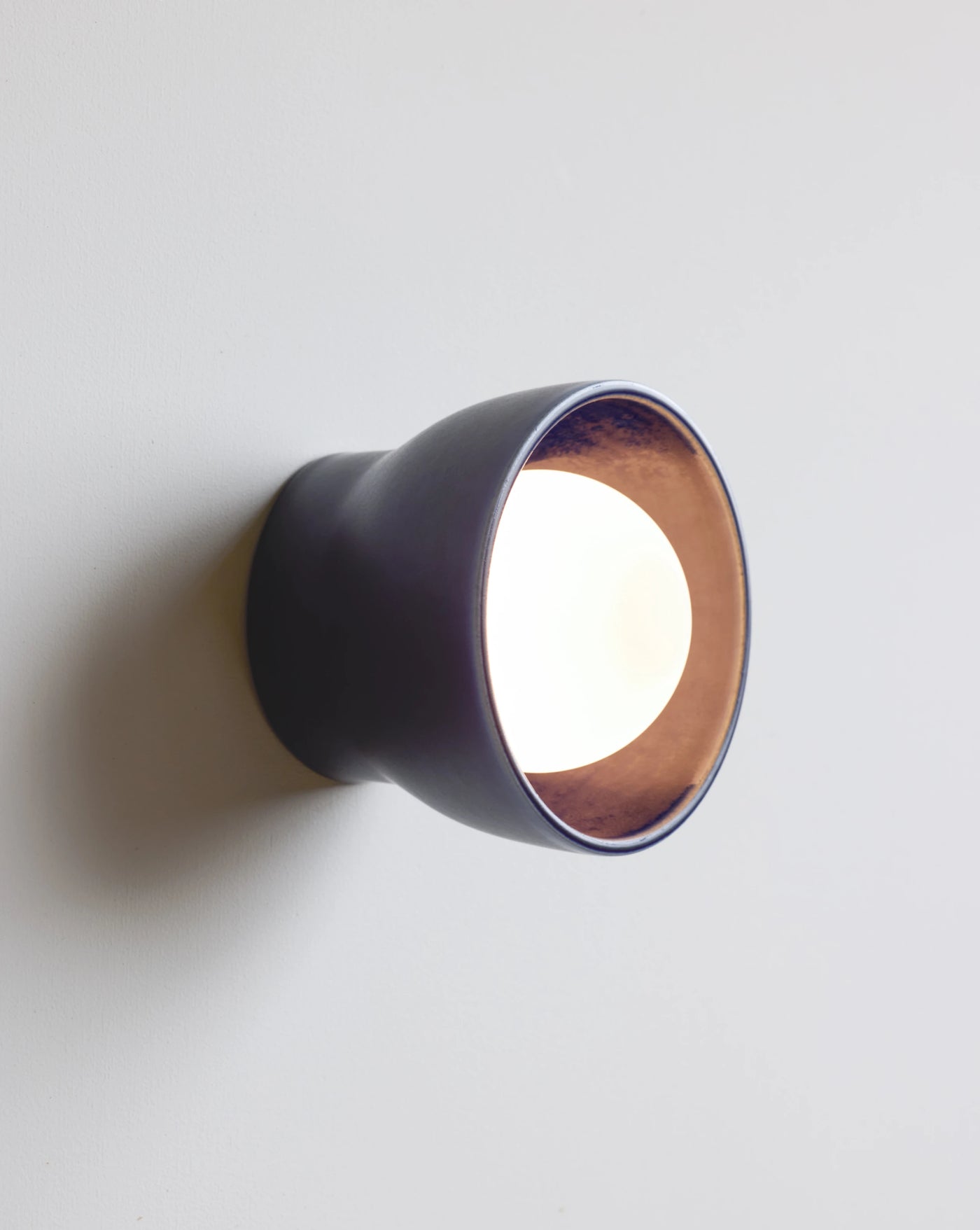 A modern wall-mounted light fixture with a dark navy exterior shown illuminated against a plain light gray wall.