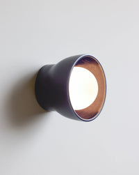 A modern wall-mounted light fixture with a dark navy exterior shown illuminated against a plain light gray wall.