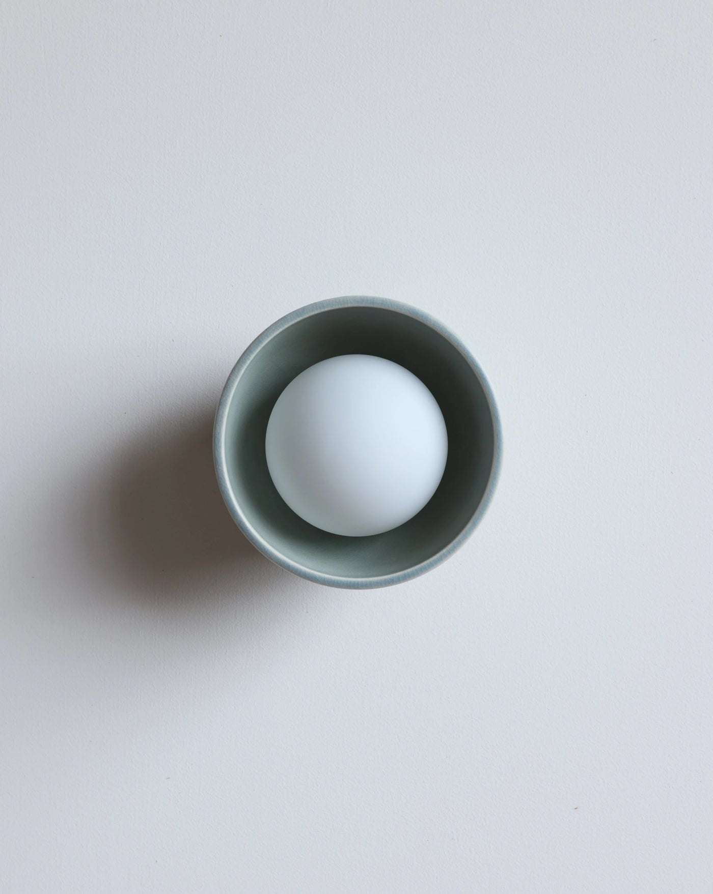 A matte sage ceramic wall sconce, photographed on a clean, light gray background.
