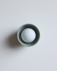 A matte sage ceramic wall sconce, photographed on a clean, light gray background.