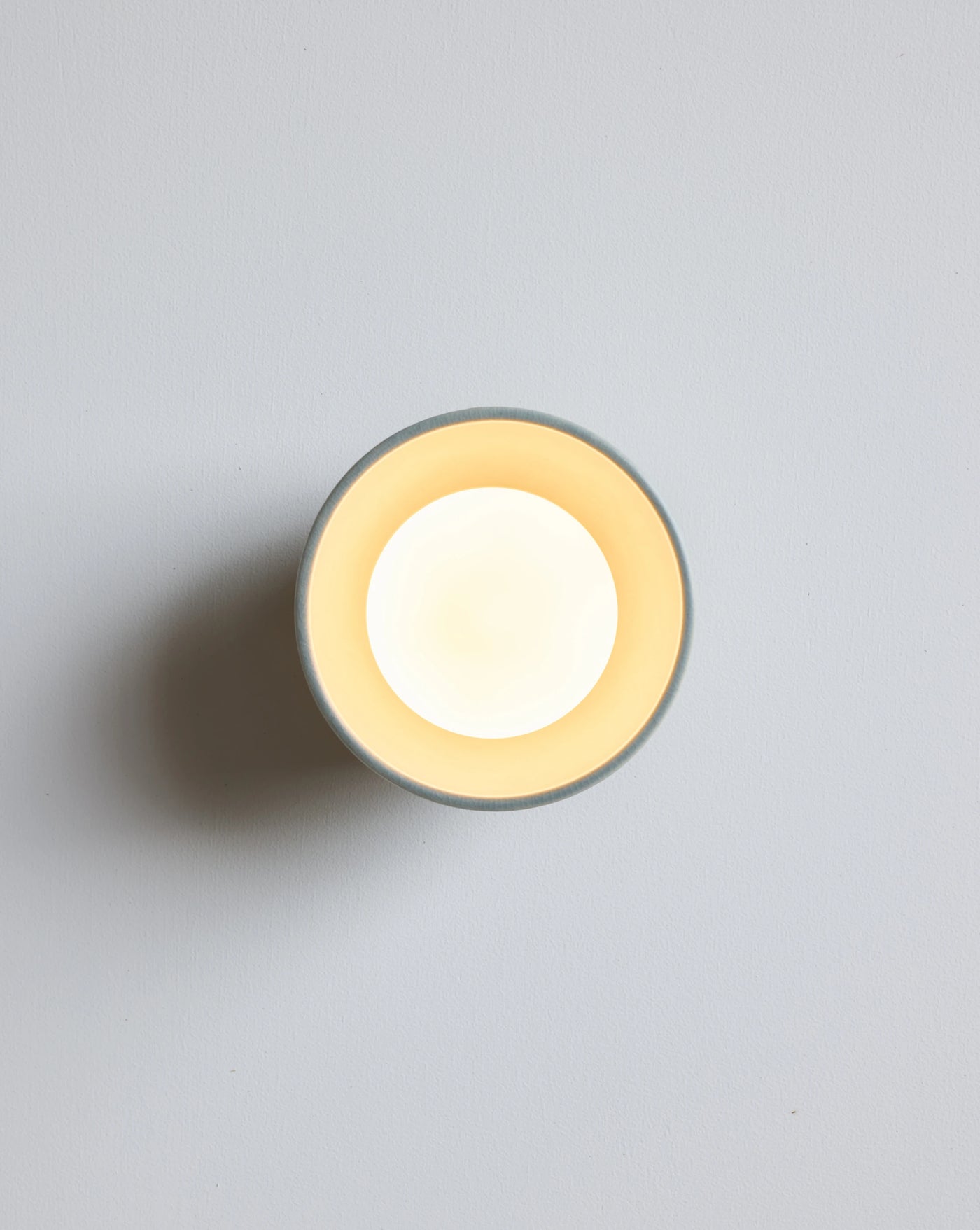 A minimalist round wall sconce light fixture shown against a light gray background.