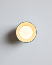 A minimalist round wall sconce light fixture shown against a light gray background.
