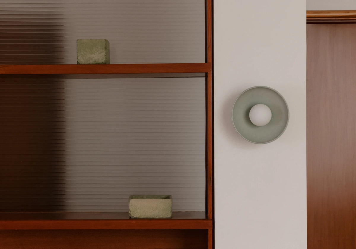 A minimalist circular wall sconce mounted on a white wall next to a wooden cabinet.