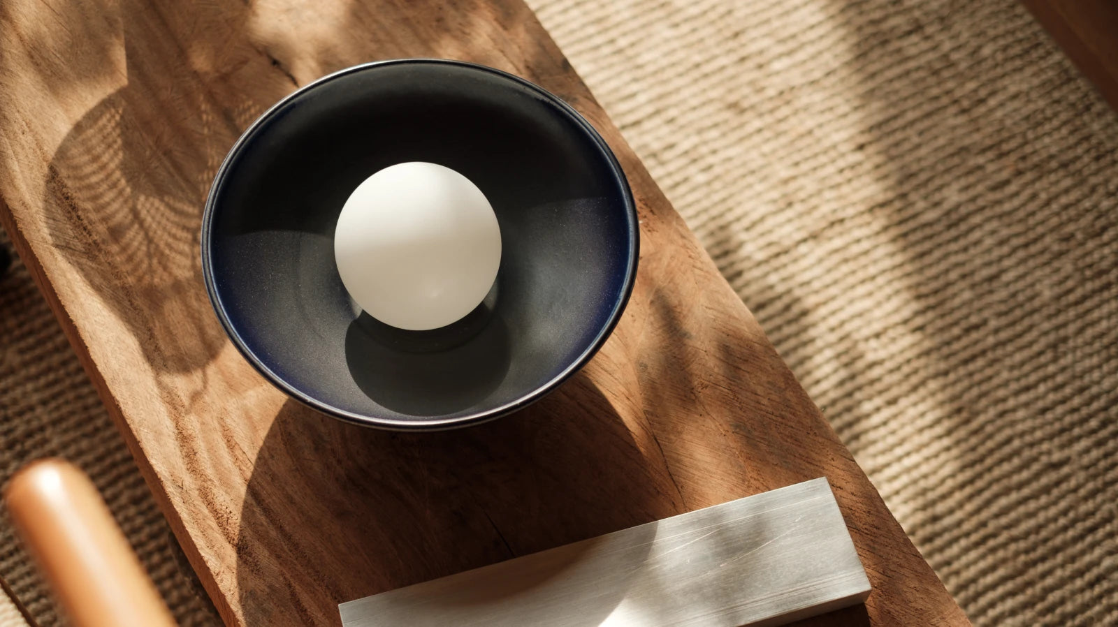 A dark navy blue ceramic sconce, styled on a rustic wooden table with natural sunlight and shadows.